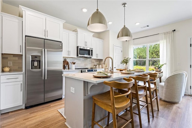 kitchen with stainless steel appliances, a sink, a kitchen island with sink, light countertops, and light wood-style flooring