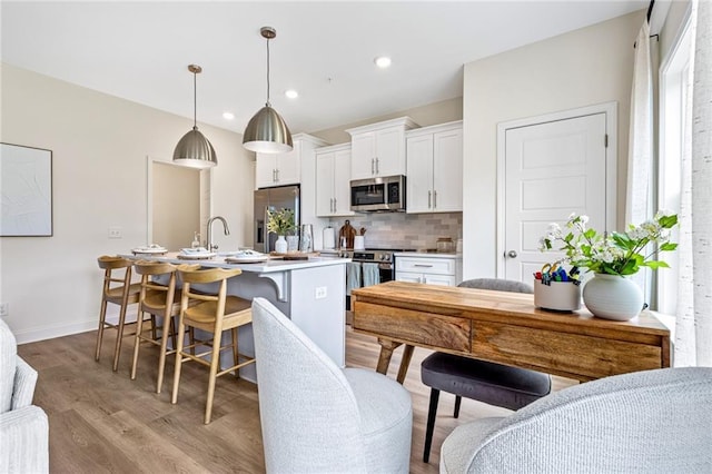 kitchen with appliances with stainless steel finishes, backsplash, white cabinetry, a breakfast bar area, and light wood-style floors
