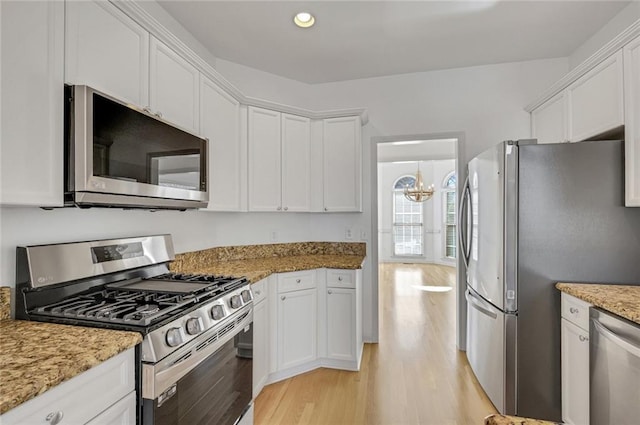 kitchen with appliances with stainless steel finishes, white cabinetry, a notable chandelier, light stone counters, and light hardwood / wood-style flooring