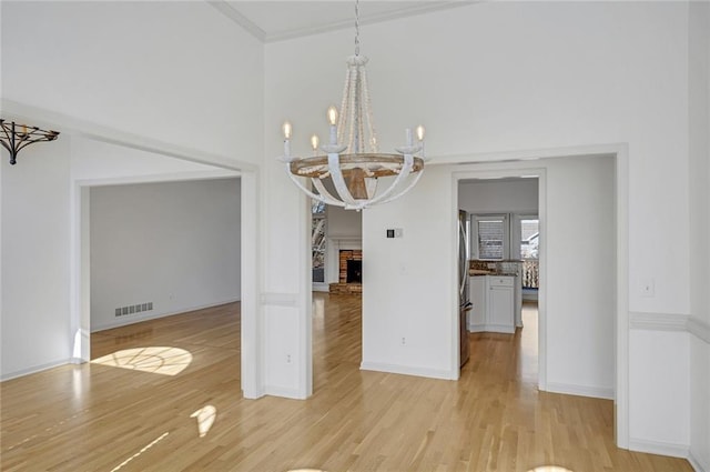 unfurnished dining area featuring an inviting chandelier, a fireplace, and light hardwood / wood-style flooring