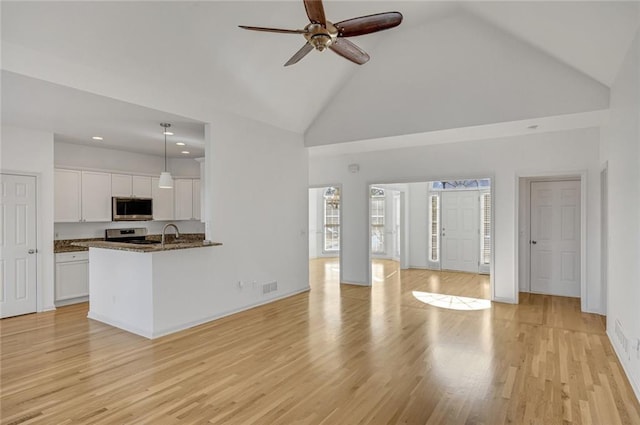 unfurnished living room with ceiling fan, sink, high vaulted ceiling, and light hardwood / wood-style flooring