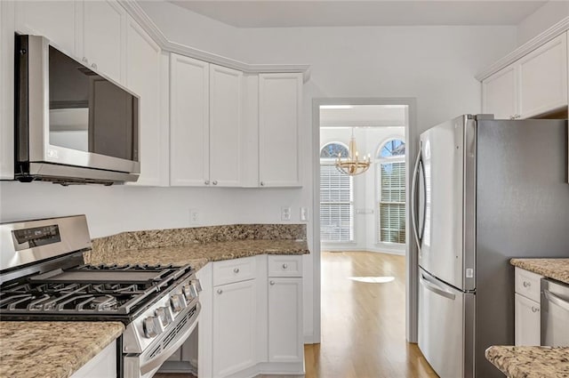 kitchen featuring white cabinetry, an inviting chandelier, light stone counters, appliances with stainless steel finishes, and light hardwood / wood-style floors