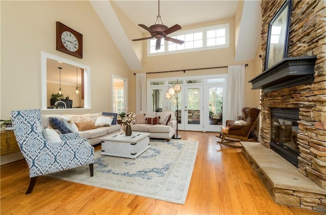 living room with ceiling fan, a stone fireplace, a high ceiling, and light wood-type flooring