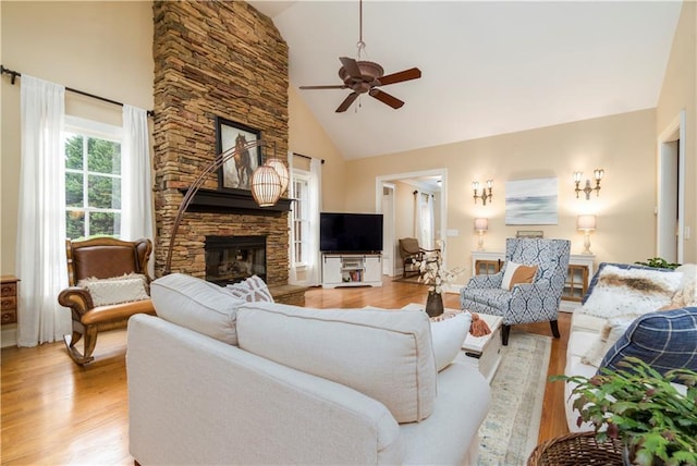 living room with ceiling fan, a fireplace, high vaulted ceiling, and light wood-type flooring