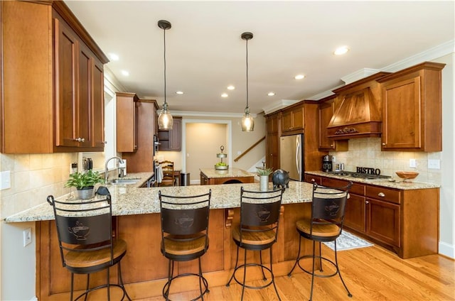 kitchen with sink, stainless steel appliances, a kitchen bar, decorative light fixtures, and custom exhaust hood