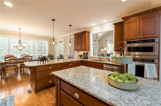 kitchen featuring sink, light stone counters, hanging light fixtures, appliances with stainless steel finishes, and kitchen peninsula