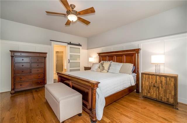 bedroom featuring ceiling fan, a barn door, connected bathroom, and light wood-type flooring