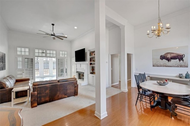 dining room featuring a fireplace with raised hearth, ornamental molding, light wood-style floors, baseboards, and ceiling fan with notable chandelier