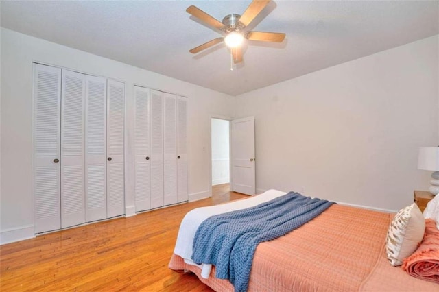 bedroom featuring light hardwood / wood-style flooring, ceiling fan, and multiple closets