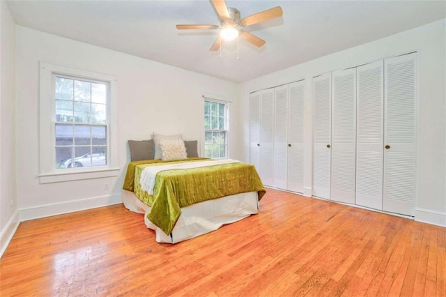 bedroom with hardwood / wood-style floors, ceiling fan, multiple closets, and multiple windows