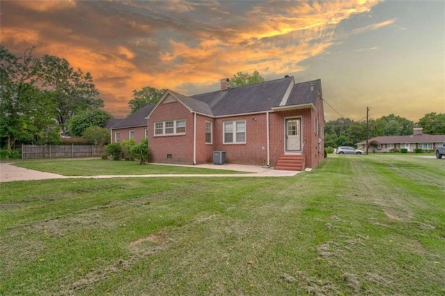 back house at dusk with a lawn and central AC unit