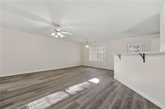 unfurnished living room with a ceiling fan, baseboards, and wood finished floors