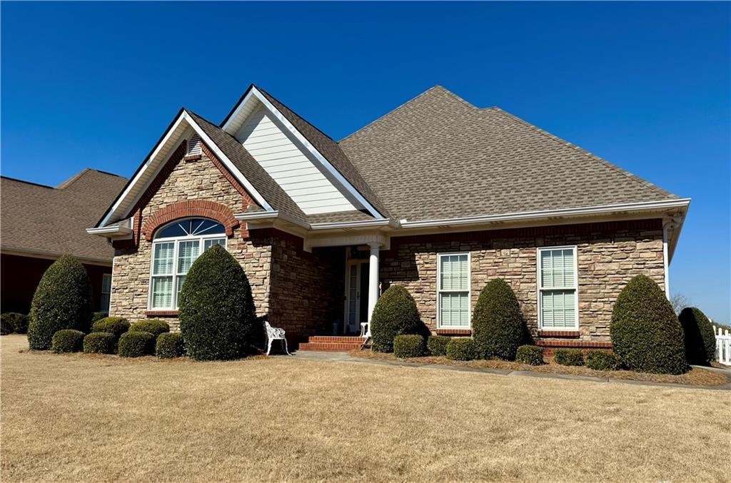 craftsman-style house with stone siding, a front lawn, and roof with shingles