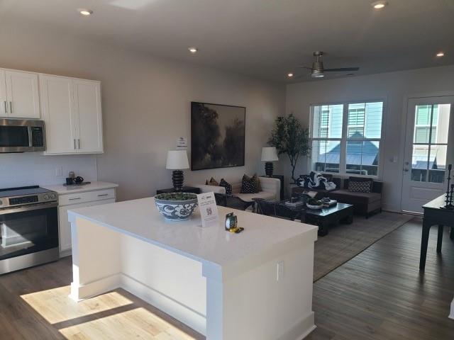 kitchen featuring a kitchen island, open floor plan, light countertops, appliances with stainless steel finishes, and dark wood finished floors