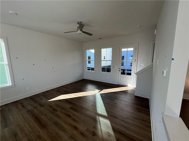 unfurnished living room with a ceiling fan, a wealth of natural light, dark wood-style flooring, and baseboards