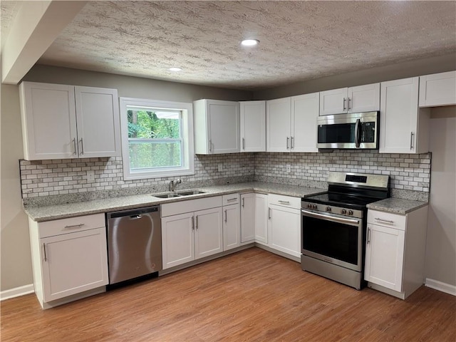1516 Chase Ct, Riverdale, GA 30296 - kitchen featuring appliances with stainless steel finishes, white cabinets, light wood-style flooring, a textured ceiling, and backsplash