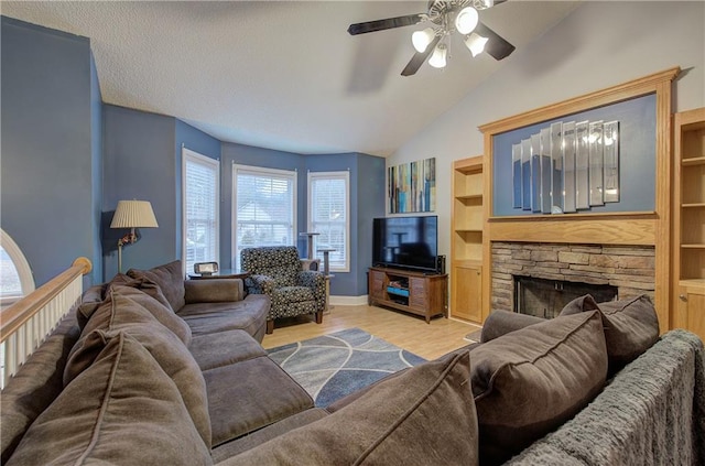 living room featuring vaulted ceiling, a stone fireplace, built in features, ceiling fan, and light hardwood / wood-style flooring