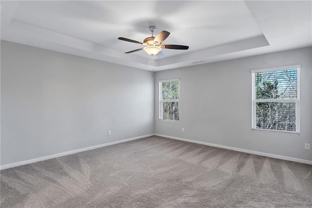 carpeted empty room featuring baseboards, a tray ceiling, and ceiling fan