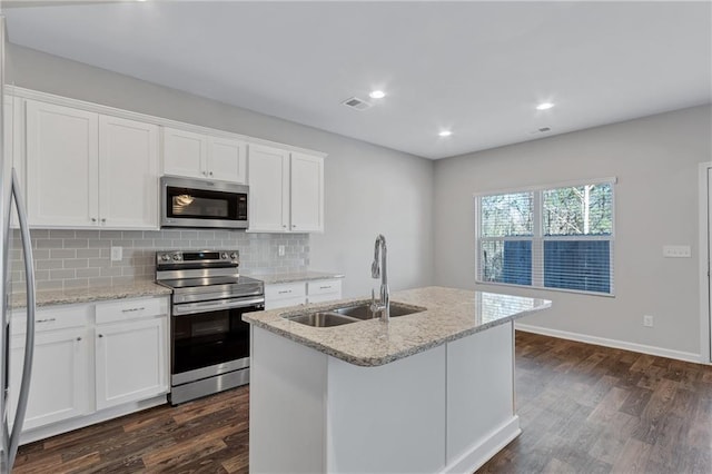 kitchen featuring a center island with sink, appliances with stainless steel finishes, white cabinets, a sink, and light stone countertops