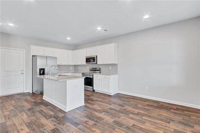 kitchen with light stone counters, dark wood-style flooring, stainless steel appliances, white cabinetry, and an island with sink