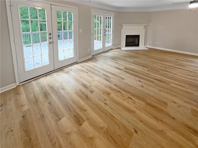 unfurnished living room with crown molding, french doors, ceiling fan, and light wood-type flooring