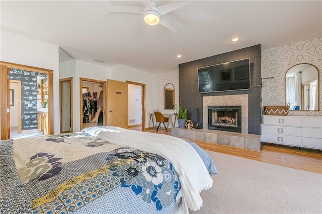 bedroom with a walk in closet, wood-type flooring, a fireplace, a closet, and ceiling fan