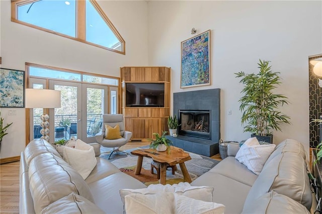 living room with french doors, light hardwood / wood-style floors, a towering ceiling, and a tile fireplace