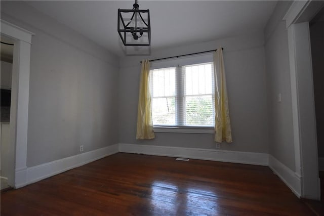 empty room featuring an inviting chandelier and dark hardwood / wood-style floors