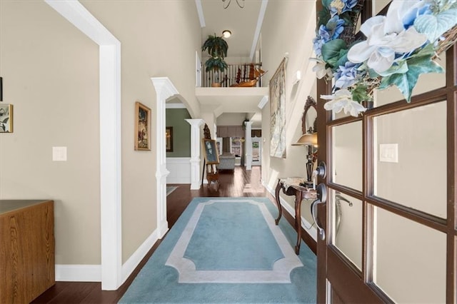 hallway featuring arched walkways, crown molding, decorative columns, a high ceiling, and wood finished floors