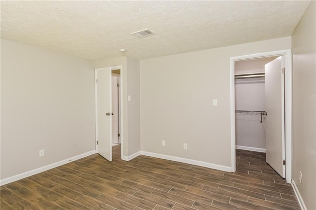 unfurnished bedroom featuring a spacious closet, a textured ceiling, and dark hardwood / wood-style flooring