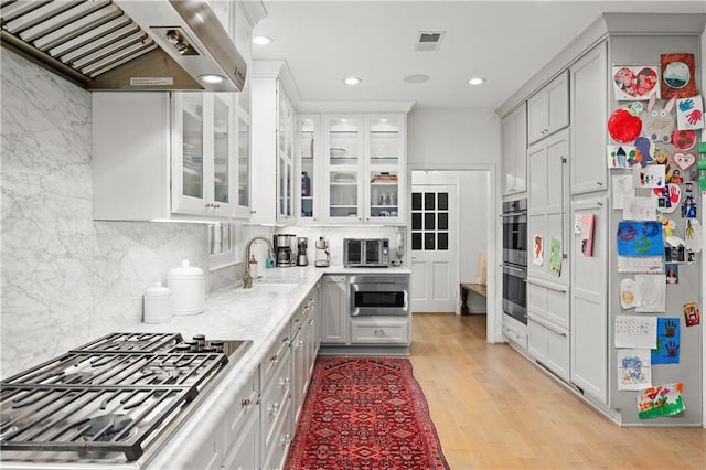 5545 Cross Gate Ct, Atlanta, GA 30327 - kitchen with appliances with stainless steel finishes, wall chimney exhaust hood, a sink, light wood-style floors, and glass insert cabinets