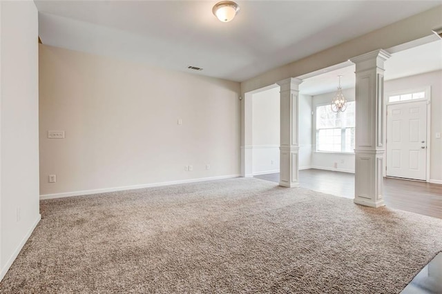 unfurnished room featuring a chandelier, dark carpet, and ornate columns