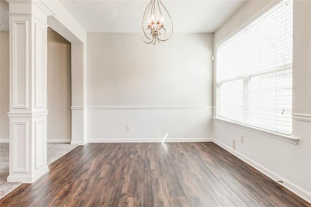 unfurnished dining area featuring a notable chandelier, a wealth of natural light, decorative columns, and dark hardwood / wood-style floors