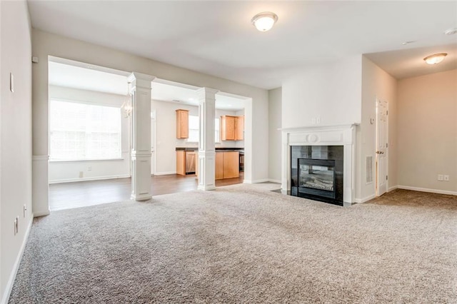 unfurnished living room with a tiled fireplace, ornate columns, and carpet flooring