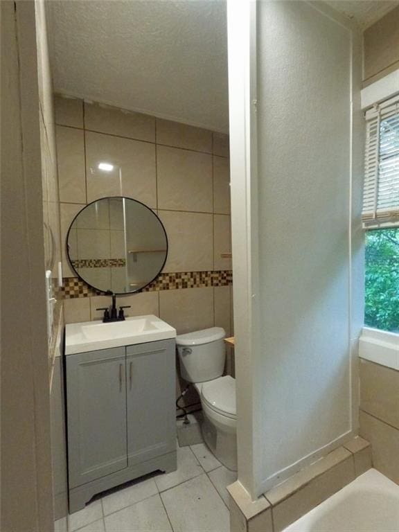 bathroom with tile patterned flooring, toilet, a bathtub, vanity, and tile walls