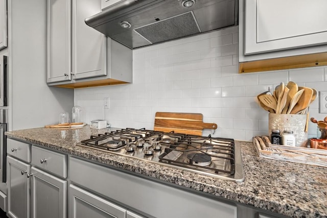 kitchen featuring tasteful backsplash, ventilation hood, dark stone countertops, gray cabinets, and stainless steel gas stovetop