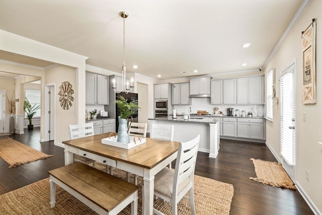 dining space with crown molding, sink, dark wood-type flooring, and a notable chandelier