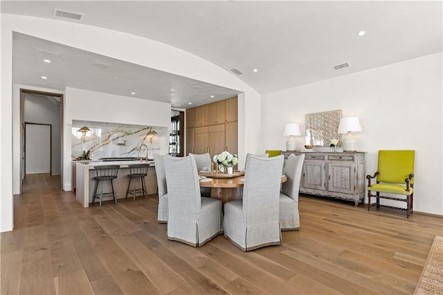 dining area with vaulted ceiling, sink, and light wood-type flooring