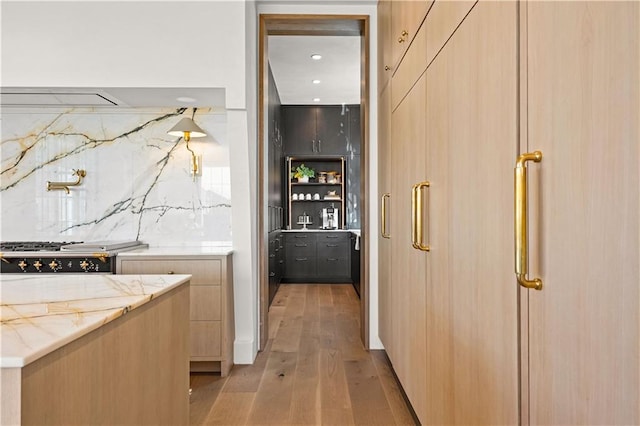 interior space featuring stove, tasteful backsplash, light stone countertops, light hardwood / wood-style floors, and light brown cabinetry