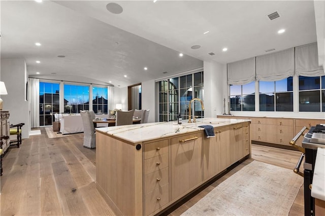 kitchen featuring light stone counters, vaulted ceiling, light hardwood / wood-style flooring, light brown cabinets, and a large island