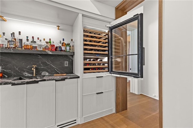 bar with backsplash, dark stone counters, light hardwood / wood-style flooring, and white cabinets