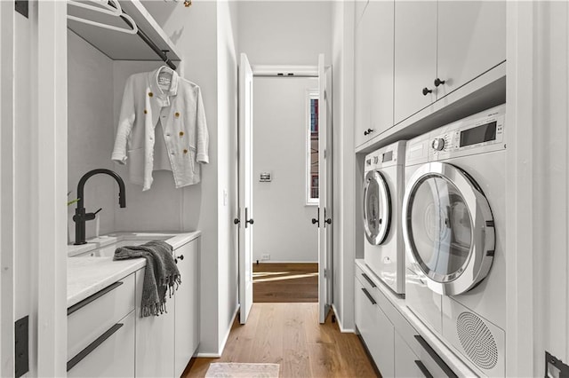 laundry area featuring sink, light hardwood / wood-style flooring, washing machine and dryer, and cabinets