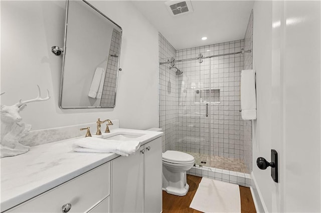 bathroom featuring vanity, wood-type flooring, a shower with shower door, and toilet