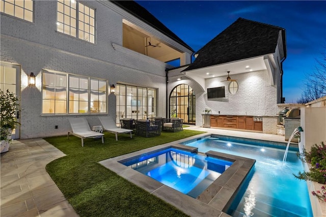 back of house with ceiling fan, a patio, an outdoor kitchen, pool water feature, and an in ground hot tub