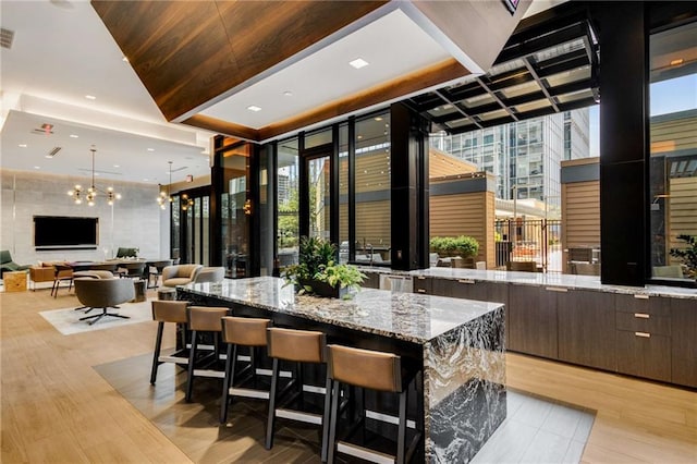 interior space with dark brown cabinetry, light stone counters, a chandelier, a spacious island, and light wood-type flooring