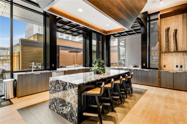 kitchen featuring a spacious island, light stone counters, a wall of windows, and light hardwood / wood-style flooring