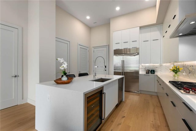 kitchen featuring appliances with stainless steel finishes, beverage cooler, sink, white cabinets, and an island with sink