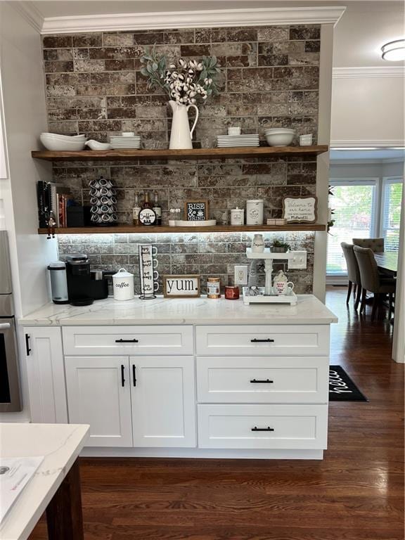 bar with dark hardwood / wood-style flooring, light stone counters, oven, ornamental molding, and white cabinetry