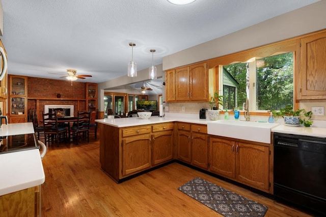 kitchen featuring kitchen peninsula, dishwasher, pendant lighting, light wood-type flooring, and sink