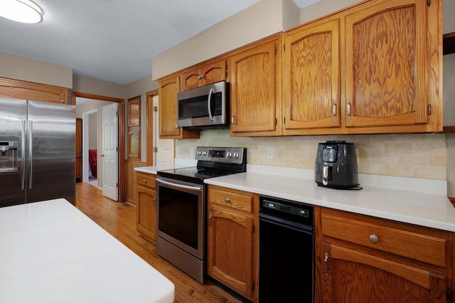 kitchen with light hardwood / wood-style flooring, stainless steel appliances, decorative backsplash, and a textured ceiling